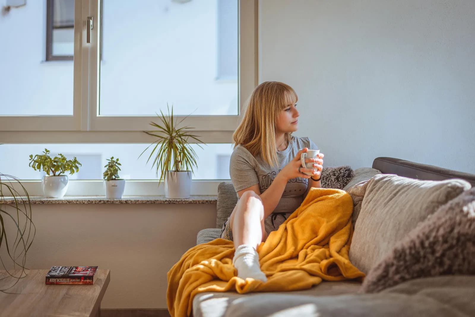 Kvinne med kaffekopp i sofaen ved et vindu